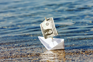 Paper boat with a dollar bill for a sail runs aground on a sandbank. Symbolize the decline of the dollar or other economic problems.